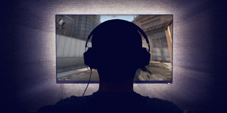 Gamer in headphones sits in front of a blank monitor in dark room